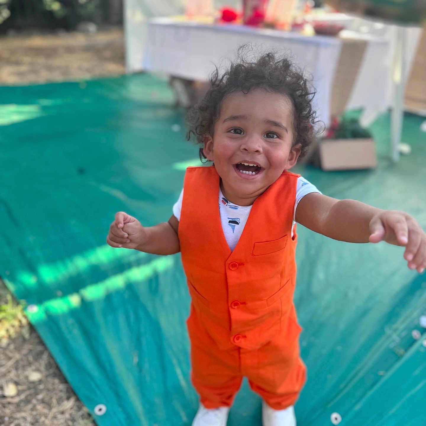 Chance is registered to the contest to win money with this photo: child, toddler, smiling, happy, outdoor, pool, poolside, swimming_pool, party, celebration, orange_outfit, vest, white_shirt, white_shoes, curly_hair, reaching, standing, portrait, summer, backyard