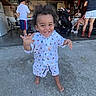 child, toddler, smiling, happy, barefoot, boy, portrait, outdoor, garage, family, gathering, stroller, chairs, concrete, playful, curly_hair, patterned_clothing, standing, people, daylight