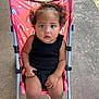 Zalaya is registered to the contest to win money with this photo: baby, black_clothing, casual, child, concrete, curious, curly_hair, cute, expression, outdoor, person, portrait, rainbow_pattern, seatbelt, sidewalk, sitting, stroller, summer, toddler, young_child