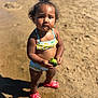 toddler, child, beach, sand, water, broccoli, swimsuit, red_shoes, curly_hair, sunlight, summer, outdoor, standing, serious_expression, young_child, nature, food, vacation, daylight, person