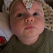 Claire is registered to the contest to win money with this photo: baby, child, face, headband, bow, sweater, green_clothing, closeup, portrait, indoor, infant, cute, soft_lighting, knitwear, texture, expression, looking_up, young_child, person, blanket