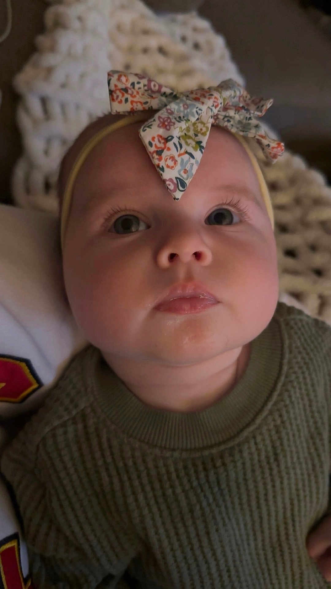 Claire is registered to the contest to win money with this photo: baby, child, face, headband, bow, sweater, green_clothing, closeup, portrait, indoor, infant, cute, soft_lighting, knitwear, texture, expression, looking_up, young_child, person, blanket