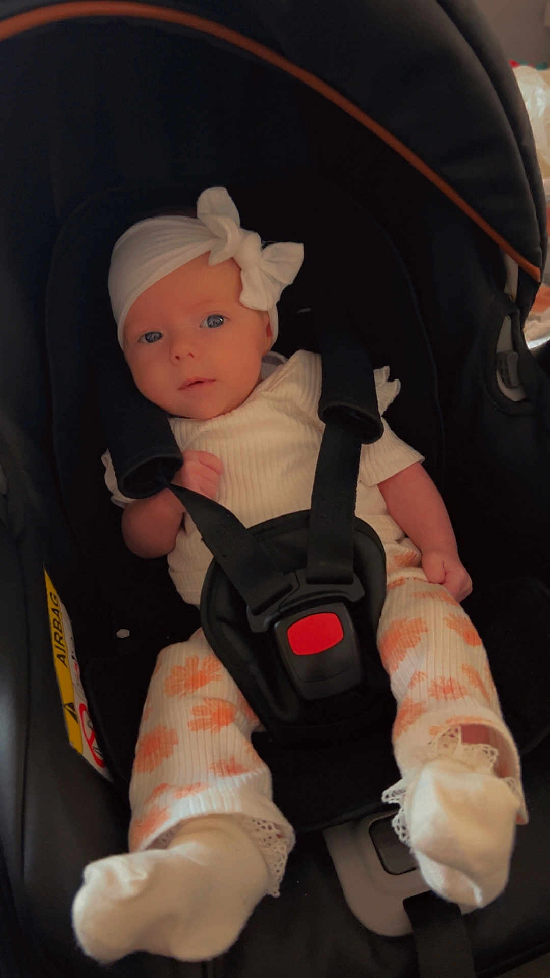 Phoebe joined the competition — help win amazing prizes! baby, infant, car_seat, headband, bow, white_clothing, orange_flower_pattern, socks, straps, black_car_seat, child, cute, indoors, portrait, small_hands, small_feet, seatbelt, looking_at_camera, soft_lighting, young_child