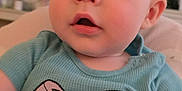 Mason is registered to the contest to win money with this photo: baby, child, infant, face, blue_shirt, cartoon_print, clothing, indoor, portrait, curious, sitting, person, young_child, cute, expression, head, eyes, mouth, skin, hair