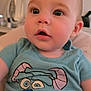 baby, child, infant, face, blue_shirt, cartoon_print, clothing, indoor, portrait, curious, sitting, person, young_child, cute, expression, head, eyes, mouth, skin, hair