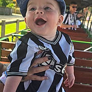 Mason is registered to the contest to win money with this photo: baby, child, smiling, happy, cap, hat, jersey, black_and_white, striped_clothing, outdoor, bench, hand, person, adult, blurred_background, daylight, greenery, fence, portrait, casual_clothing