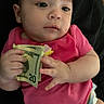 baby, cash, child, closeup, curious, cute, diaper, expression, face, hand, holding, indoors, infant, lying_down, money, person, pink_shirt, skin, twenty_dollar_bills, young_child