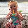 baby, child, sippy_cup, smiling, sitting, indoors, playful, carpet, colorful, toy, happy, cute, infant, person, young_child, mouth, face, hand, legs, casual_clothing