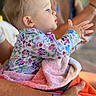 Hazel is registered to the contest to win money with this photo: baby, child, person, adult, woman, towel, watch, hand, floral_clothing, colorful, smile, portrait, indoor, holding, curious, focus, skin, hair, sitting, blurred_background