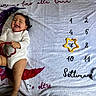 baby, infant, smiling, milestone_blanket, numbers, heart_shape, yellow_star, white_clothing, lying_down, celebration, months, cute, child, happy, headband, colorful, fabric, pattern, text, photography