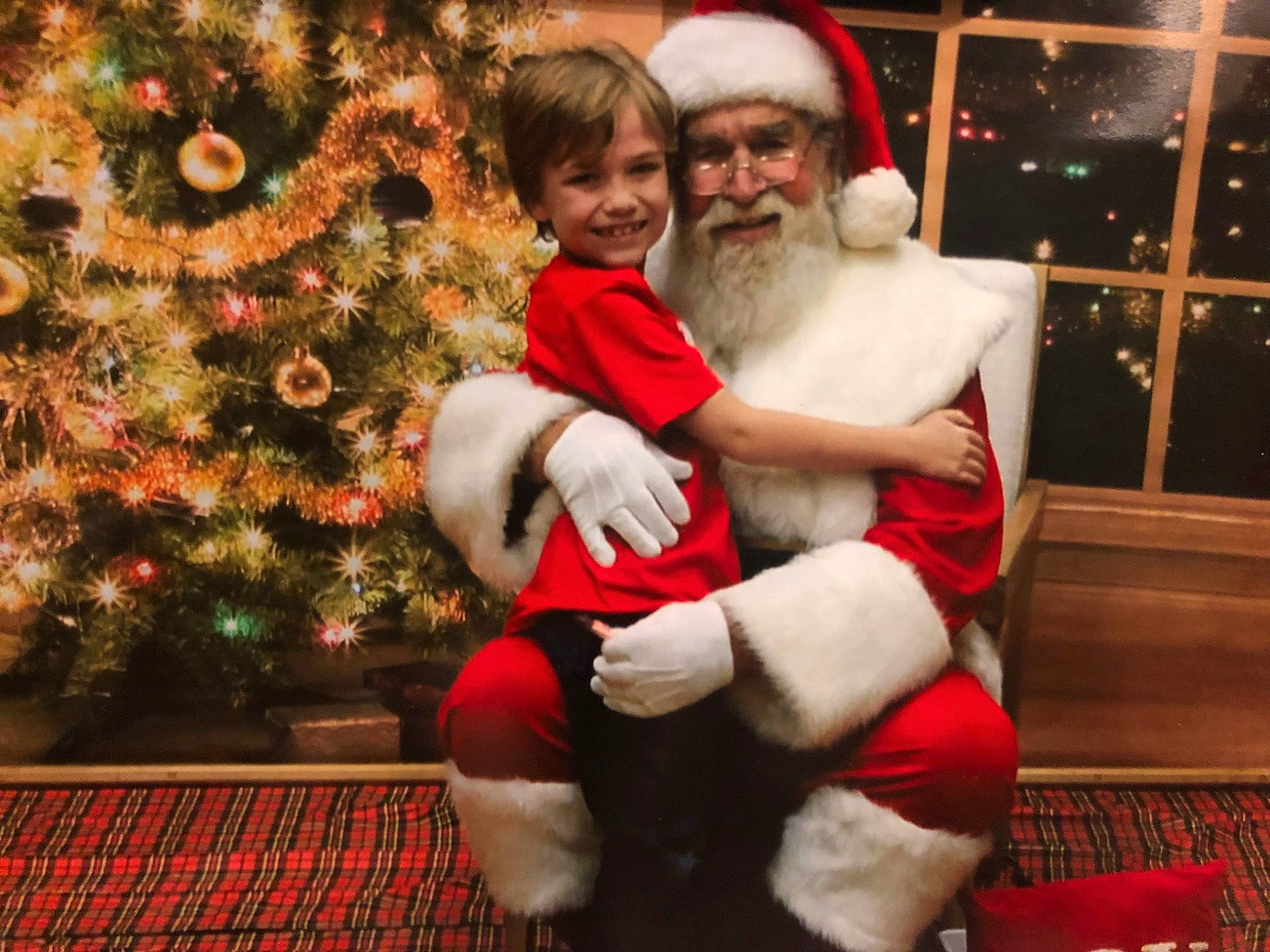 Abel is registered to the contest to win money with this photo: beard, christmas, christmas_decoration, christmas_eve, christmas_ornament, christmas_tree, event, facial_expression, facial_hair, fun, happy, hat, headwear, holiday, human_body, joy, lap, person, photograph, red