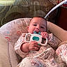 Rosetta is registered to the contest to win money with this photo: baby, infant, teething_toy, cushion, animal_print, floral_pajamas, hand, face, indoor, soft_toys, comfort, seat, child, person, cute, relaxing, closeup, head, expression, home