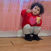 Amer is registered to the contest to win money with this photo: child, toddler, curly_hair, red_sweater, heart_design, ice_cream_cone, peace_sign, pink_curtain, golden_pattern, wooden_floor, black_boots, gray_pants, indoor, cute, happy, portrait, sitting, playful, smiling, cozy