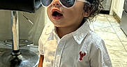 Timothy joined the competition — help win amazing prizes! child, toddler, portrait, sunglasses, standing, kitchen, indoors, white_shirt, button_up_shirt, shorts, curly_hair, open_mouth, barstool, sink, cabinets, tile_floor, home, fashion, posing, smiling