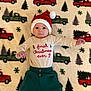 baby, child, christmas, holiday, festive, hat, santa_hat, blanket, pattern, trucks, christmas_trees, clothing, pants, cute, infant, smiling, lying_down, indoors, portrait, celebration