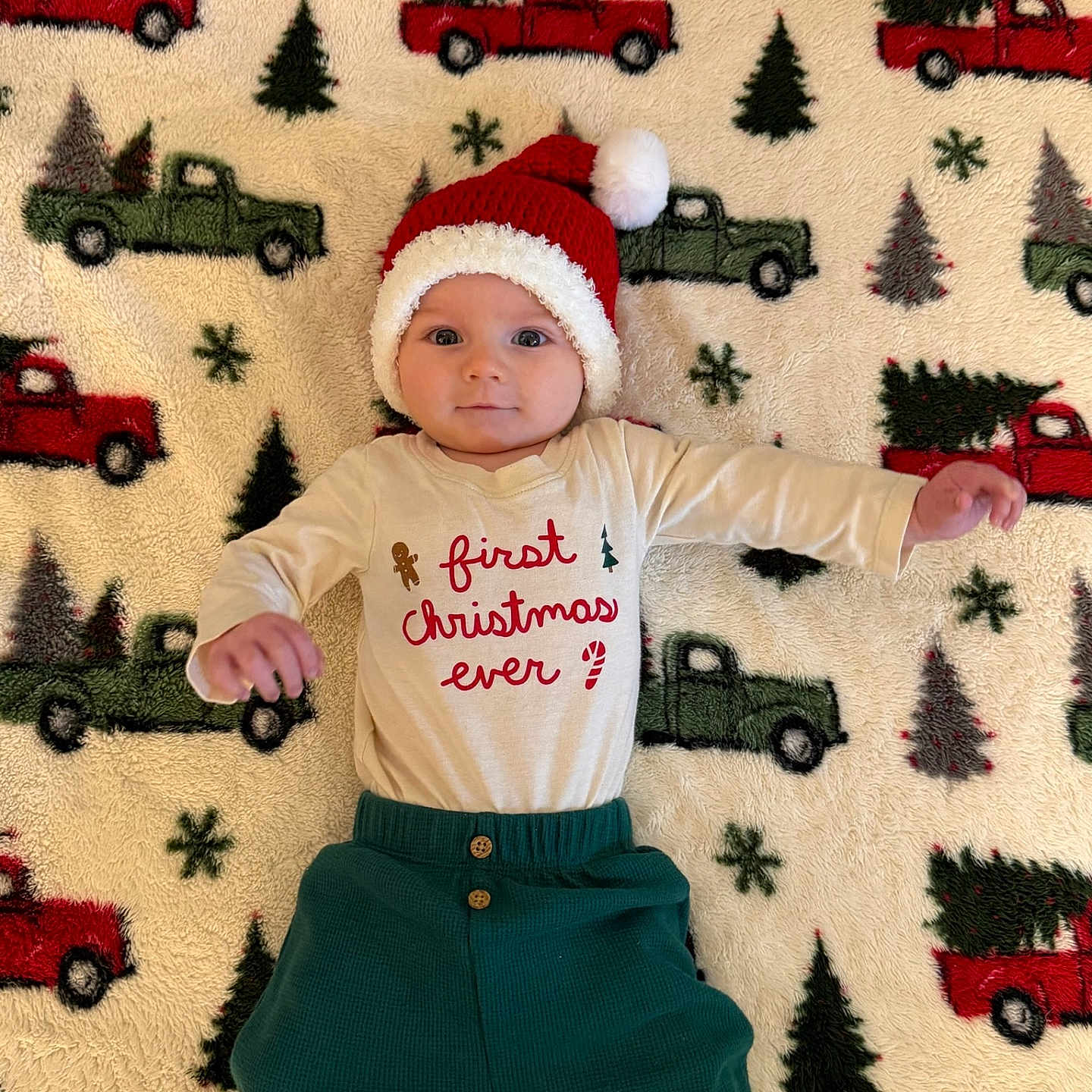 Bohdie is registered to the contest to win money with this photo: baby, blanket, celebration, child, christmas, christmas_trees, clothing, cute, festive, hat, holiday, indoors, infant, lying_down, pants, pattern, portrait, santa_hat, smiling, trucks