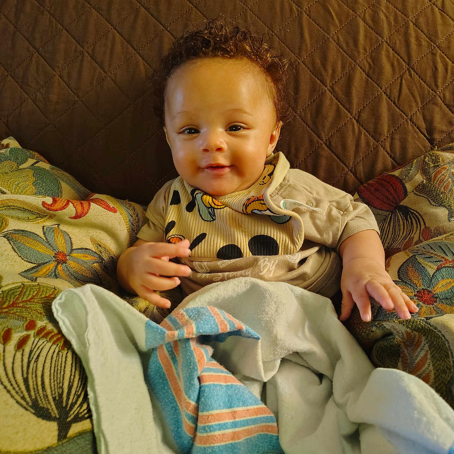 Samuel joined the competition — help win amazing prizes! baby, child, smile, curly_hair, blanket, pillow, indoor, cute, face, infant, clothing, person, happy, portrait, toddler, cozy, soft, sitting, home, comfort