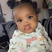 Zahara joined the competition — help win amazing prizes! toddler, child, baby, pajamas, floral_pattern, hair_buns, face, expression, indoor, blanket, seated, cute, playful, room, door, furniture, person, portrait, warm, cozy