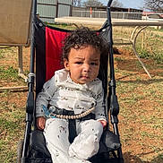 Roman joined the competition — help win amazing prizes! child, baby, stroller, curly_hair, onesie, pacifier, seatbelt, outdoor, grass, dirt, sky, clouds, table, chair, chain_link_fence, power_lines, face, kolcraft_logo, wheel, sitting
