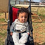 child, baby, stroller, curly_hair, onesie, pacifier, seatbelt, outdoor, grass, dirt, sky, clouds, table, chair, chain_link_fence, power_lines, face, kolcraft_logo, wheel, sitting