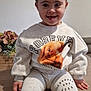 toddler, child, smile, sitting, sweatshirt, leggings, hair_buns, portrait, indoor, table, flower_arrangement, framed_photos, cute, happy, clothing, young_child, family, casual, cozy, home