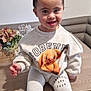 Isla joined the competition — help win amazing prizes! child, toddler, smiling, indoor, sitting, sweatshirt, leggings, hair_buns, cute, face, table, plant, couch, home, decor, clothing, portrait, happy, person, cozy