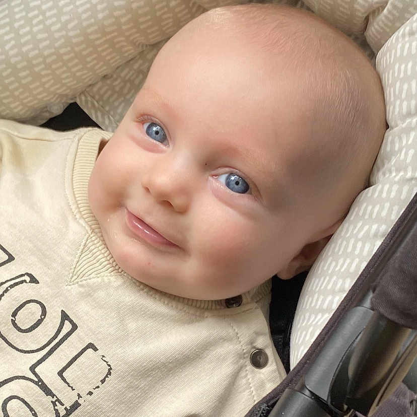 Leo is registered to the contest to win money with this photo: baby, blue_eyes, smile, stroller, cushion, cream_clothing, infant, face, head, child, cute, outdoor, person, portrait, happy, young, baby_clothes, seat, closeup, cozy