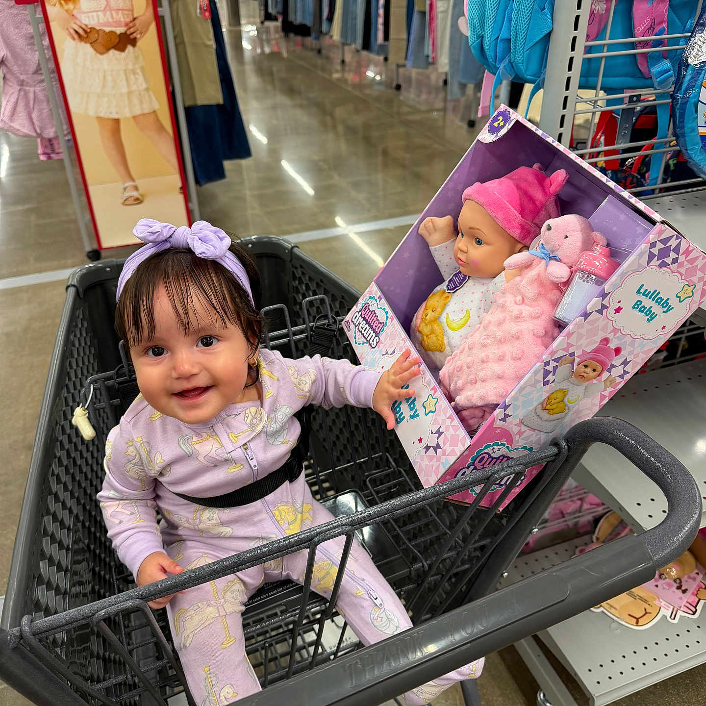 Georgina joined the competition — help win amazing prizes! baby, child, shopping_cart, toy_store, doll, boxed_toy, smiling, happy, infant, purple_clothing, headband, indoor, retail_store, clothing_racks, backpacks, store_aisle, portrait, shopping, cardboard_display, family_outing