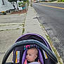 baby, car_seat, blanket, sidewalk, street, suburban, outdoor, child, infant, purple, curious, daylight, residential, person, road, house, nature, walk, expression, safety