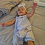 baby, infant, bed, blanket, clothing, headband, arm, smile, cute, romper, strawberry_print, baby_wipes, fabric, person, child, indoor, soft_light, reaching, comfort, toddler