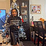 Ivy participe au concours pour gagner de l'argent avec cette photo : child, girl, christmas_tree, holiday, decorations, living_room, sweater, leather_skirt, boots, braided_hair, necklace, cabinet, photo_frame, ornament, tree_star, smile, portrait, furniture, floor, television