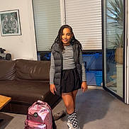 Ivy participe au concours pour gagner de l'argent avec cette photo : child, girl, backpack, living_room, couch, window, open_door, plant, sneakers, checkered_socks, striped_shirt, puffer_vest, skirt, braids, portrait, smile, floor, painting, indoor, home