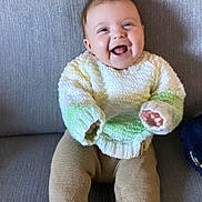 Joey joined the competition — help win amazing prizes! baby, child, smiling, sweater, knitwear, pants, sitting, couch, indoor, happy, face, person, infant, young_child, cozy, cute, portrait, clothing, home, seated
