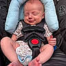 baby, infant, car_seat, child, smiling, face, headrest, safety_harness, clothing, onesie, floral_pattern, feet, hands, sleepy, comfort, seat, baby_accessory, cute, peaceful, portrait