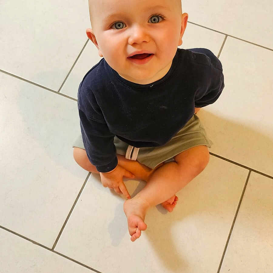 Jules participe au concours pour gagner de l'argent avec cette photo : baby, barefoot, blue_eyes, casual_clothing, child, cross_legged, curious, cute, floor, indoor, long_sleeve, looking_up, person, short_hair, shorts, sitting, smile, tile, toddler, young_child