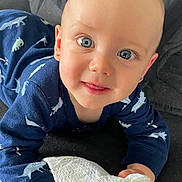 Jaxxon is registered to the contest to win money with this photo: baby, blue_eyes, crawling, dinosaur_print, blue_outfit, cloth, cute, face, child, infant, smiling, indoors, closeup, person, small_hands, soft_toy, blanket, head, happy, toddler
