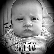Luca is registered to the contest to win money with this photo: baby, infant, face, portrait, black_and_white, clothing, striped, onesie, text_on_clothing, bow_tie, expression, serious, close_up, person, child, young, cute, indoors, monochrome, head