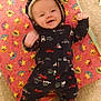 baby, infant, smiling, onesie, hooded_clothing, blanket, patterned_blanket, carpet, indoor, happy, child, lying_down, cute, raised_fists, colorful, star_pattern, toy_pattern, foot, face, person