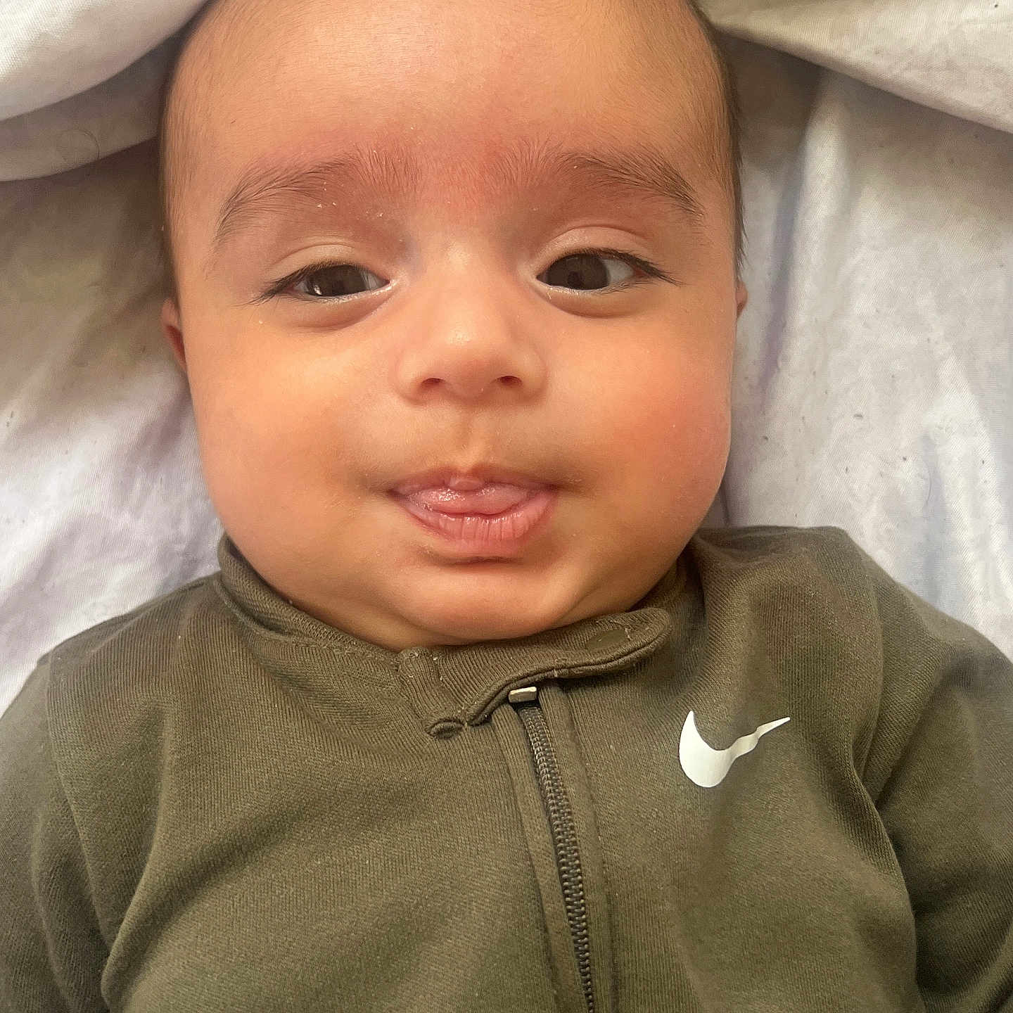 Rovan joined the competition — help win amazing prizes! baby, infant, child, portrait, face, eyes, looking_at_camera, lying_down, onesie, clothing, olive_green, nike_logo, blanket, bedding, soft_lighting, indoors, close_up, adorable, neutral_expression, head