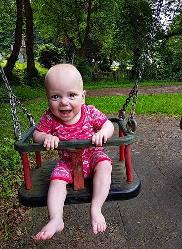 Rupert is registered to the contest to win money with this photo: baby, child, fun, joy, outdoor_play_equipment, person, pink, play, playground, product, public_space, recreation, sitting, smile, swing, toddler, tree