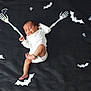 baby, sleeping, infant, white_clothing, black_background, skeleton_arms, cartoon_bats, halloween_theme, cute, peaceful, lying_down, decorations, playful, indoors, soft_lighting, child, footwear_absent, dark_fabric, holiday, festive