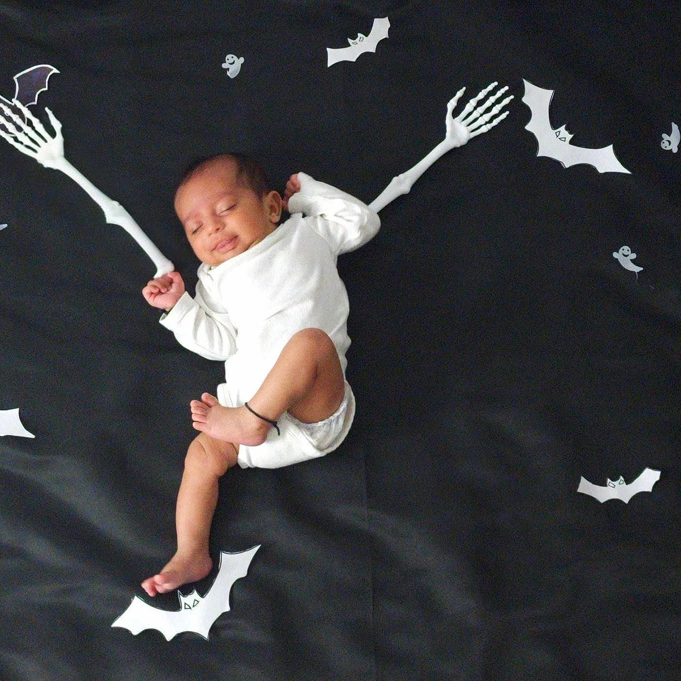 Eshan joined the competition — help win amazing prizes! baby, black_background, cartoon_bats, child, cute, dark_fabric, decorations, festive, footwear_absent, halloween_theme, holiday, indoors, infant, lying_down, peaceful, playful, skeleton_arms, sleeping, soft_lighting, white_clothing