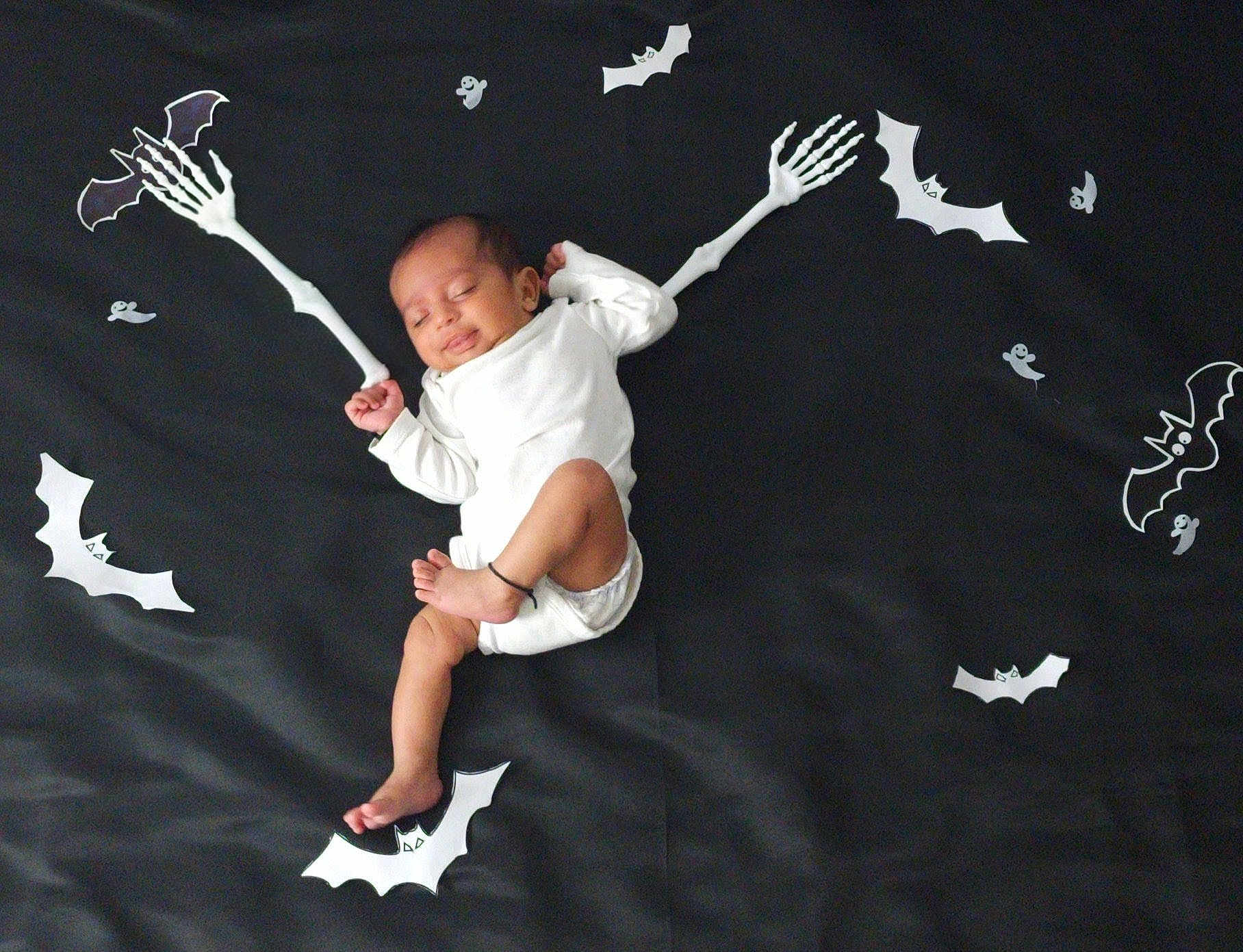 Eshan joined the competition — help win amazing prizes! baby, sleeping, infant, white_clothing, black_background, skeleton_arms, cartoon_bats, halloween_theme, cute, peaceful, lying_down, decorations, playful, indoors, soft_lighting, child, footwear_absent, dark_fabric, holiday, festive