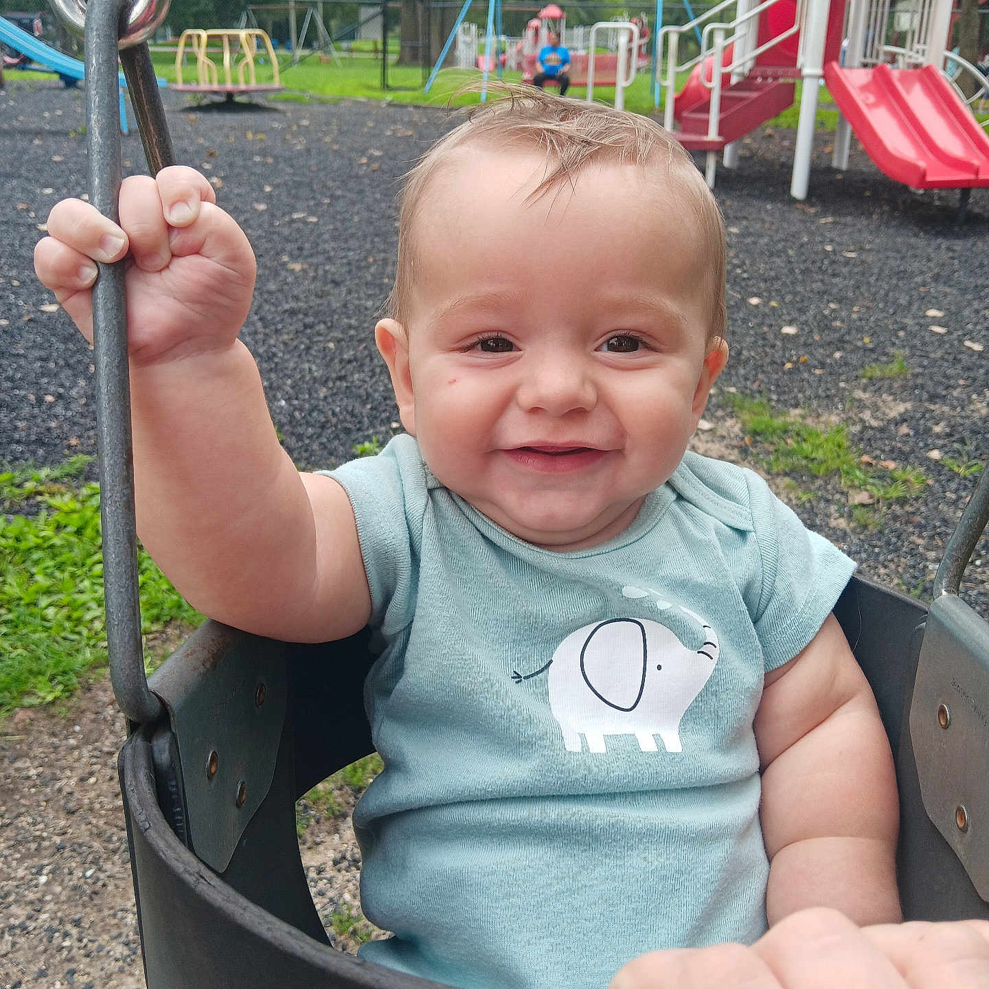 Tyrael is registered to the contest to win money with this photo: baby, child, swing, playground, smiling, elephant_print, shirt, hand, outdoor, grass, slide, play_equipment, metal_chain, happy, young_child, daylight, park, person, nature, fun
