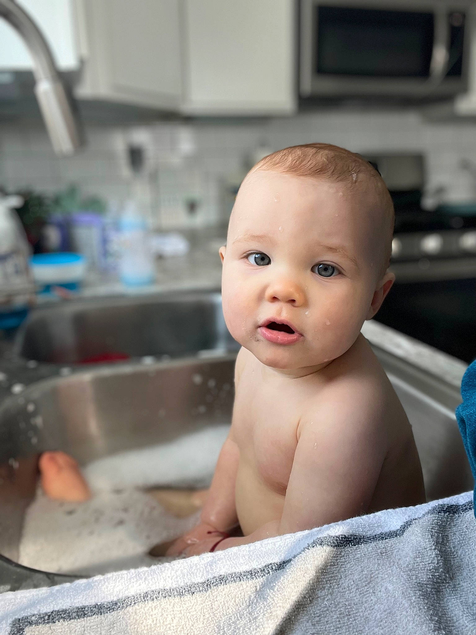 Westin is registered to the contest to win money with this photo: baby, baby_bathing, bathing, blue, cabinetry, cheek, chest, child, flooring, fluid, fun, home_appliance, kitchen, kitchen_appliance, person, plumbing_fixture, sink, skin, tap, toddler