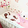 baby, crib, mobile, toy, blanket, pillow, child, infant, smiling, sleeping_area, nursery, decor, pink, white, floral_pattern, bunny, soft_toys, floor, clothing, person