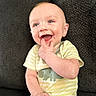 Kendall is registered to the contest to win money with this photo: baby, child, smiling, happy, couch, clothing, onesie, dinosaur, blue_eyes, fingers, mouth, skin, person, sitting, infant, cute, indoor, texture, fabric, portrait
