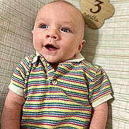 Kendall is registered to the contest to win money with this photo: baby, infant, child, blue_eyes, striped_shirt, colorful_clothing, plaid_blanket, wooden_sign, milestone, portrait, smiling, happy, cute, lying_down, close_up, face, skin, short_hair, indoors, young_child