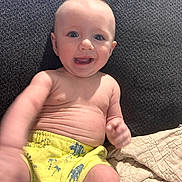Kendall is registered to the contest to win money with this photo: baby, smiling, child, happy, couch, yellow_shorts, blue_patterns, bare_chest, quilt, indoor, person, infant, reaching, cute, portrait, skin, young, seated, texture, home