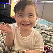 Sebastian is registered to the contest to win money with this photo: bed, blanket, child, clothing, curtain, expression, face, furniture, hair, hand, happy, home, indoor, light, person, quilt, room, smiling, toddler, window